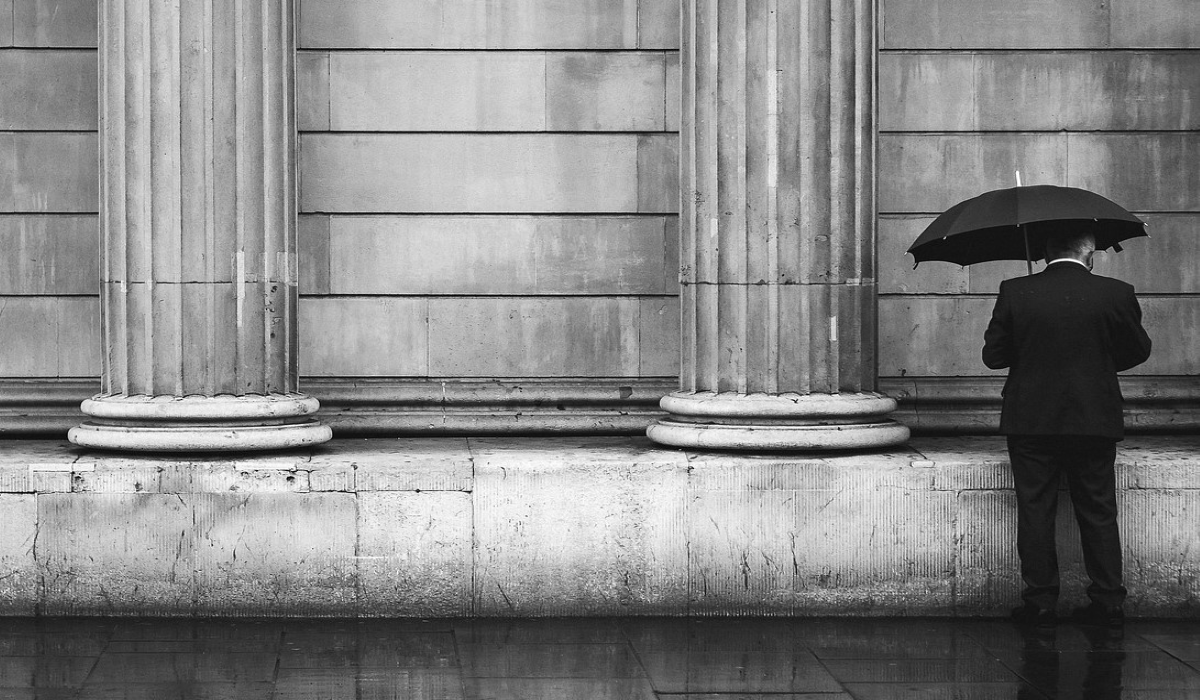 Man in black with an umbrella standing next to classic roman pillars