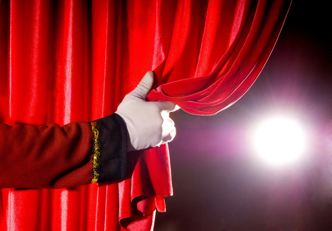 Hand pulling a red curtain open backstage with light starting to pour in