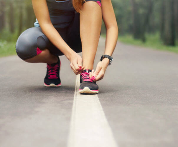 Runner bends down to tie their shoe on a forest-lined path