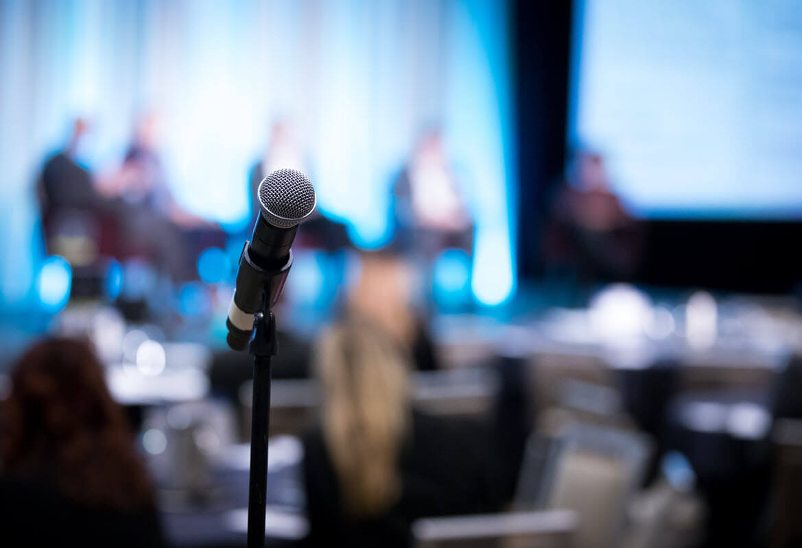 Close up of microphone on a stand with blurred-out background of a shareholder meeting