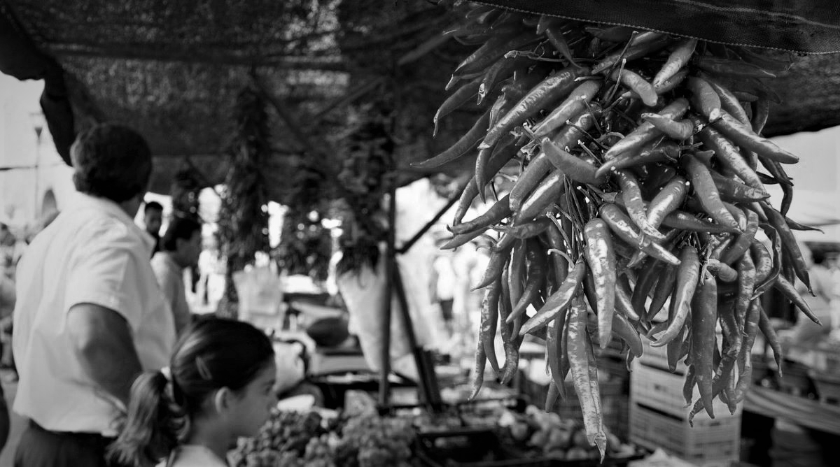 An outdoor produce market with hanging bunches of chilies