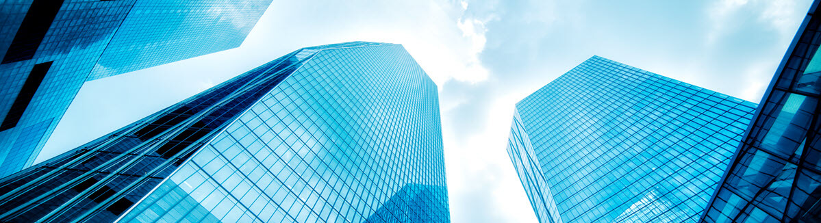 Photograph of skyscrapers with glass windows from the ground facing up to a blue sky