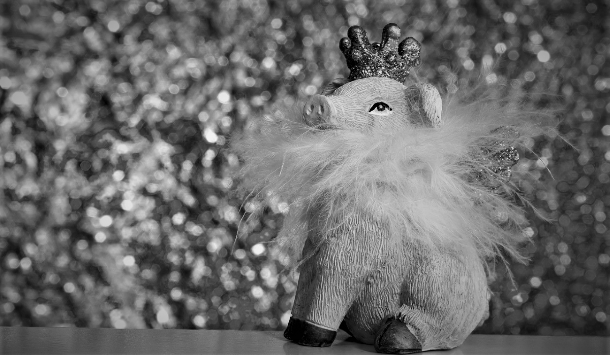 Toy pig with wings, wearing a feather boa and a crown, sits on the edge of a table