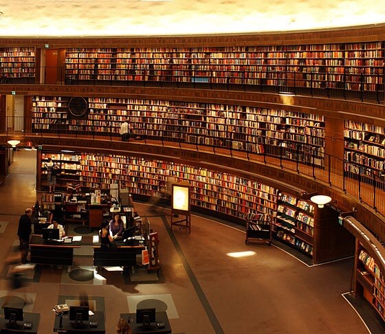 Circular library with 3 levels of bookshelves and rotunda in the center with desks and working people