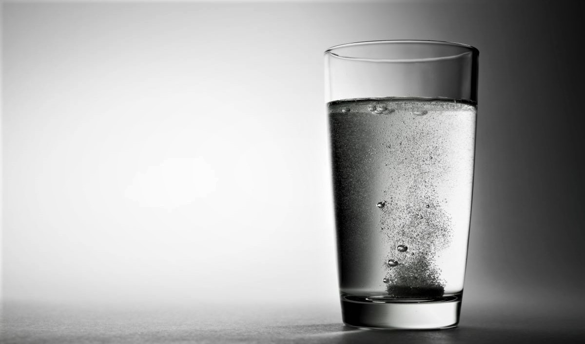 An antacid tablet fizzles in the bottom of a glass of water