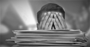 A large stack of files piled up in front of a person, showing only the top of his head