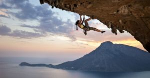 Rock climber climbs on an overhang with a large body of water and mountain in the background
