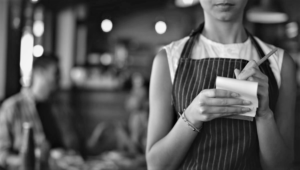 An annoyed-looking server takes a restaurant patron's order